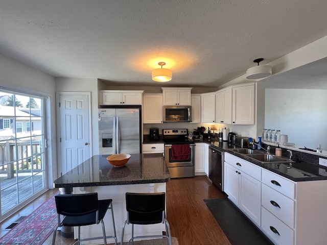 kitchen with appliances with stainless steel finishes, a center island, a sink, white cabinets, and dark wood-style floors