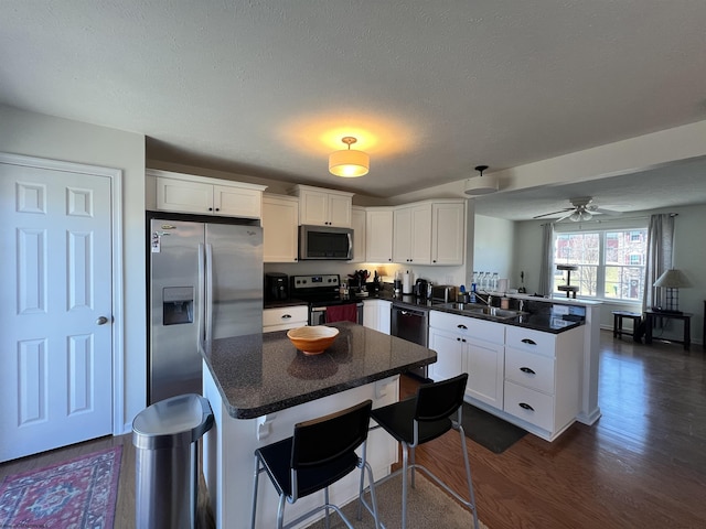 kitchen featuring a peninsula, white cabinetry, appliances with stainless steel finishes, and dark wood-style floors