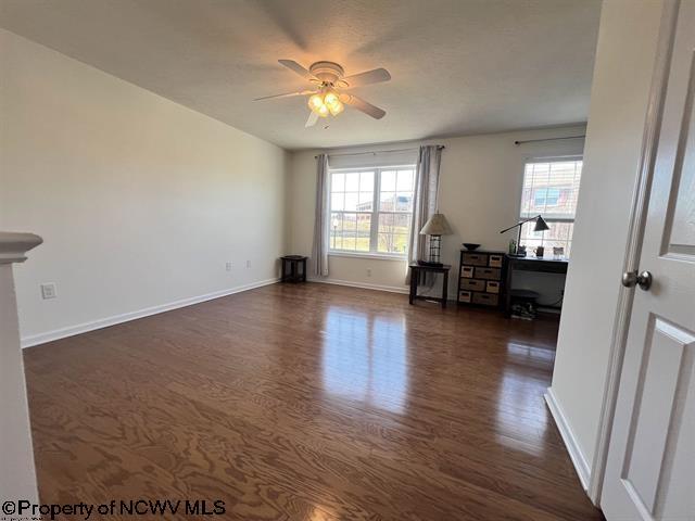 unfurnished room featuring baseboards, a ceiling fan, and dark wood finished floors