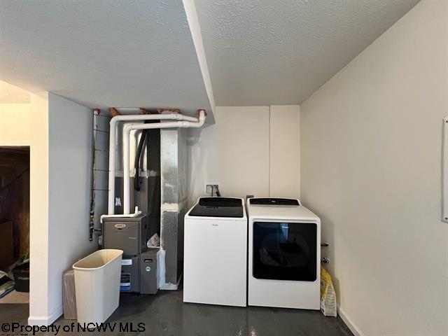 washroom with laundry area, a textured ceiling, baseboards, heating unit, and washer and dryer