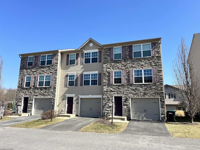 townhome / multi-family property featuring driveway, stone siding, and a garage