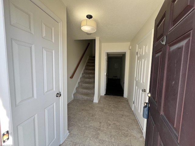 foyer featuring stairs, a textured ceiling, baseboards, and stone finish flooring