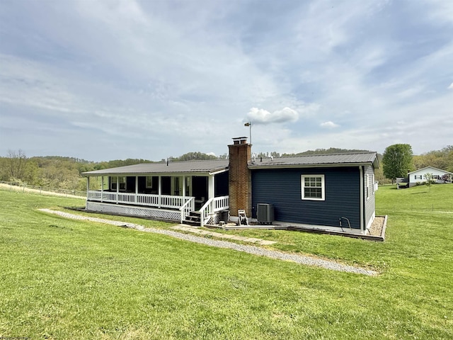 back of house with central air condition unit, covered porch, a chimney, and a lawn