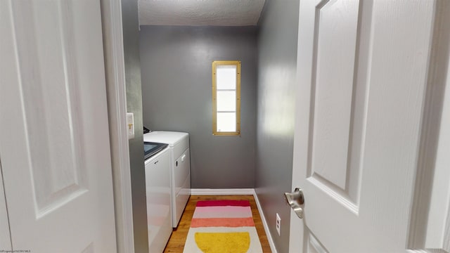 laundry room with laundry area, baseboards, light wood-type flooring, a textured ceiling, and independent washer and dryer