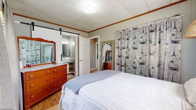 bedroom with crown molding, light wood-style floors, and a barn door