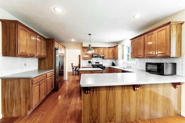 kitchen featuring a peninsula, under cabinet range hood, brown cabinets, a sink, and stainless steel appliances