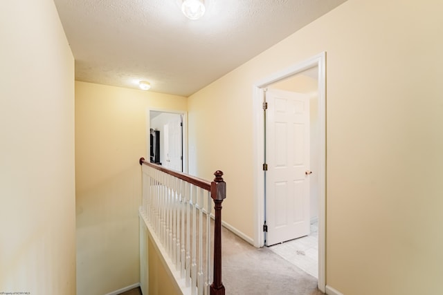 hall with baseboards, carpet flooring, a textured ceiling, and an upstairs landing