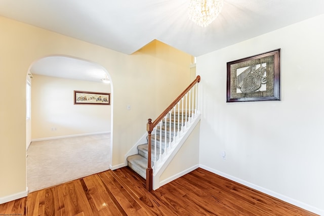 stairway with an inviting chandelier, arched walkways, baseboards, and wood finished floors