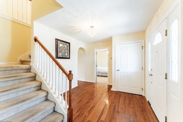 entryway with an inviting chandelier, baseboards, stairway, arched walkways, and light wood finished floors