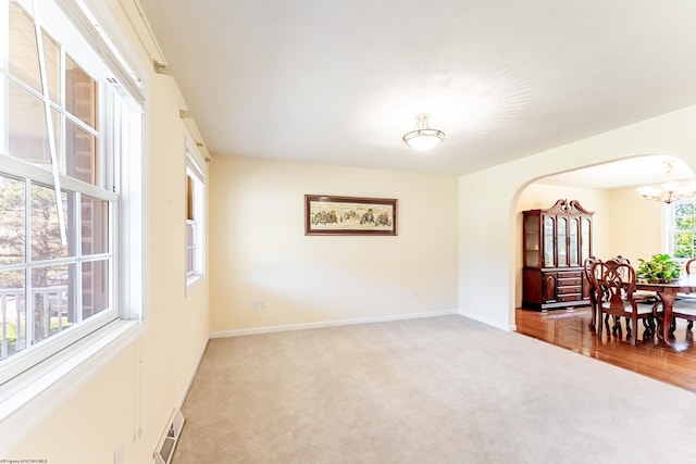 carpeted spare room with an inviting chandelier, arched walkways, baseboards, and visible vents