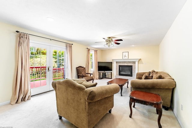 living area featuring a glass covered fireplace, baseboards, light colored carpet, french doors, and a ceiling fan