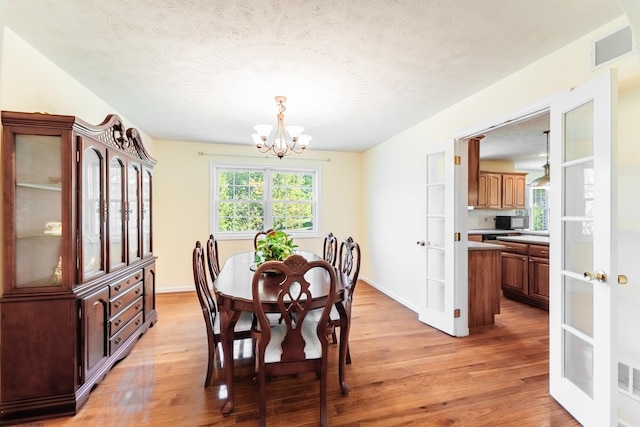 dining room with visible vents, light wood-style flooring, baseboards, and a notable chandelier