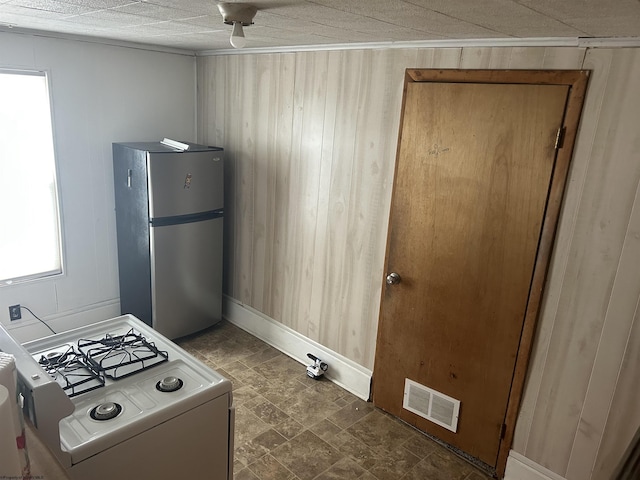 kitchen featuring visible vents, freestanding refrigerator, wood walls, and gas range