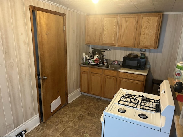 kitchen featuring visible vents, black microwave, gas range gas stove, wooden walls, and a sink
