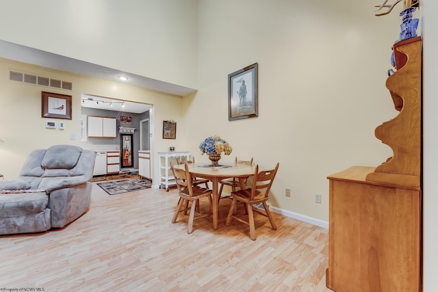 dining space with visible vents, track lighting, baseboards, a high ceiling, and light wood finished floors