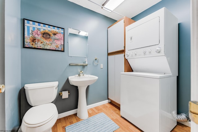 bathroom featuring baseboards, toilet, stacked washer / dryer, and wood finished floors