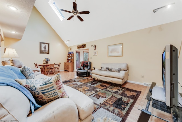 living area with baseboards, ceiling fan, high vaulted ceiling, light wood-style flooring, and a skylight