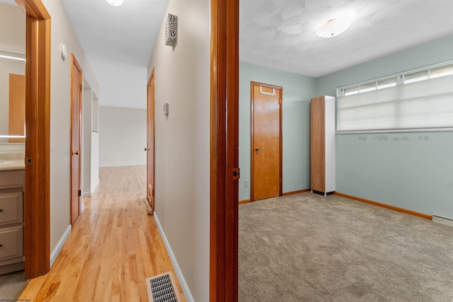 corridor with visible vents, baseboards, and light wood-type flooring