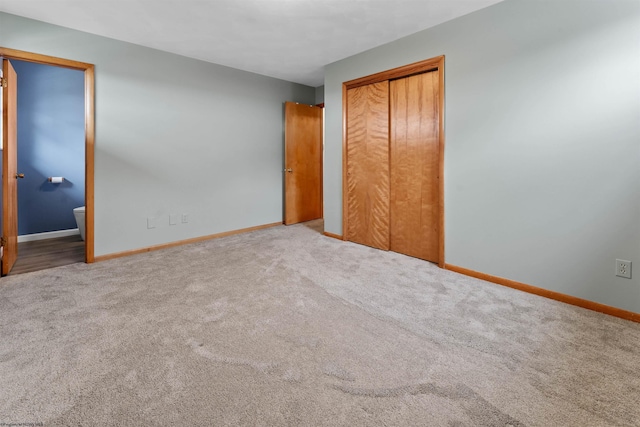 unfurnished bedroom featuring carpet floors, baseboards, a closet, and ensuite bath