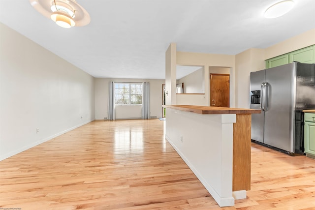 kitchen with stainless steel fridge, baseboards, green cabinetry, and light wood finished floors