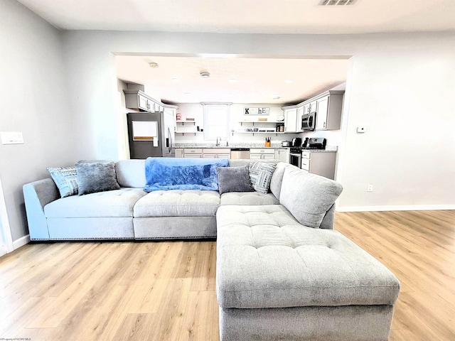 living area with visible vents, light wood-style floors, and baseboards