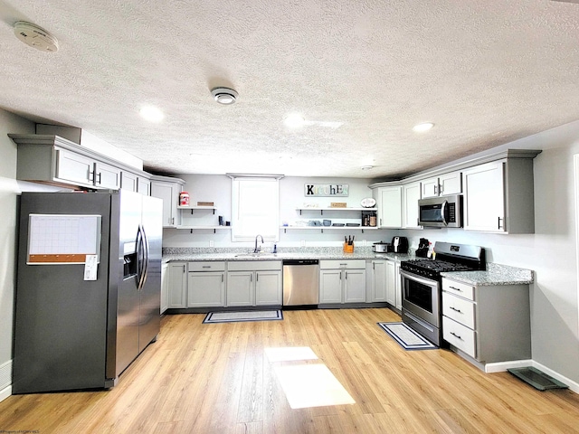 kitchen with open shelves, a sink, a textured ceiling, and stainless steel appliances