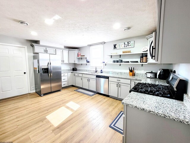 kitchen with open shelves, light stone countertops, a sink, a textured ceiling, and stainless steel appliances