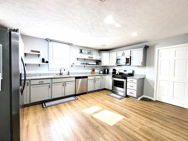 kitchen featuring a sink, open shelves, stainless steel appliances, and a textured ceiling