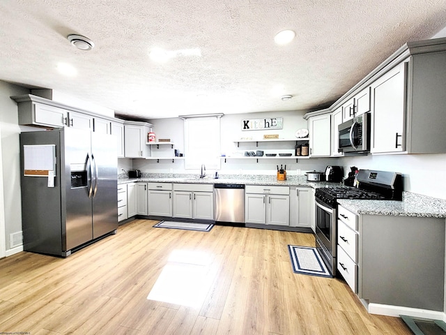 kitchen with a textured ceiling, open shelves, appliances with stainless steel finishes, and light wood finished floors