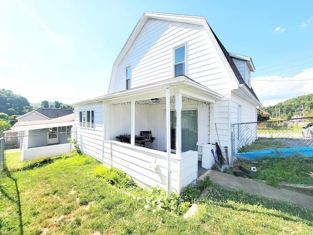 view of side of home featuring a lawn, fence, and a gambrel roof