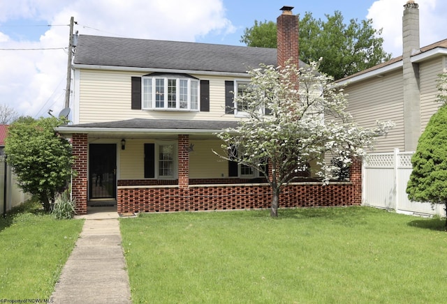view of front facade featuring brick siding, a front lawn, fence, and covered porch