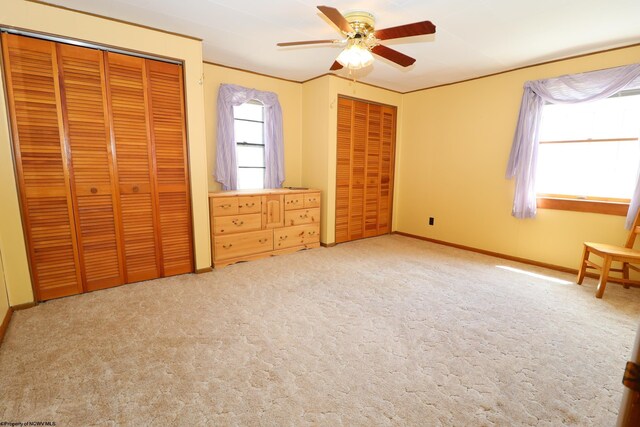 unfurnished bedroom featuring baseboards, carpet, multiple closets, and ceiling fan