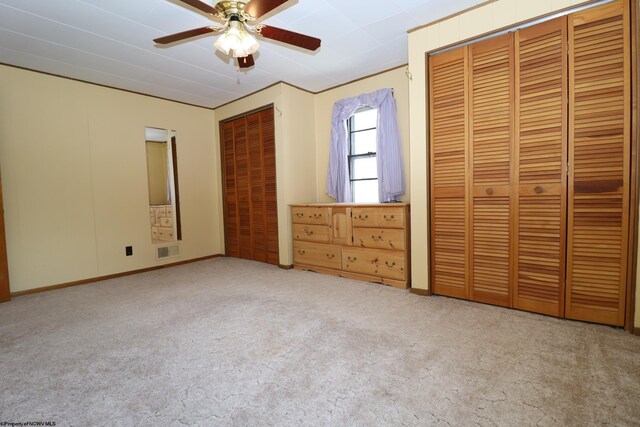 unfurnished bedroom with multiple closets, carpet, a ceiling fan, and visible vents