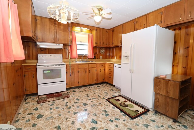 kitchen with brown cabinets, a sink, light countertops, under cabinet range hood, and white appliances