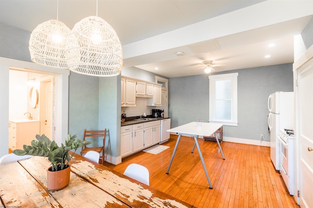 kitchen featuring decorative backsplash, light wood-type flooring, a sink, baseboards, and white appliances