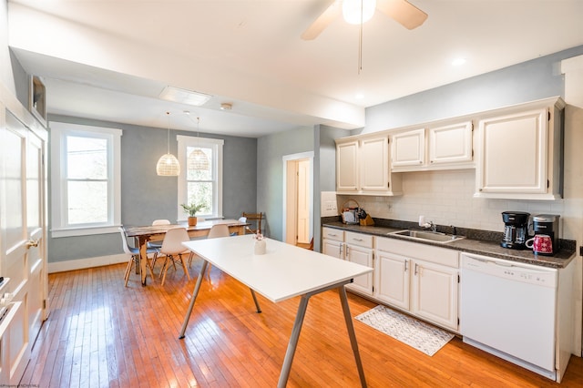 kitchen featuring white dishwasher, dark countertops, a sink, light wood-style floors, and backsplash