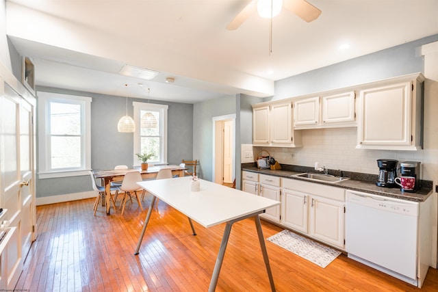 kitchen with white dishwasher, dark countertops, tasteful backsplash, a sink, and light wood-style flooring