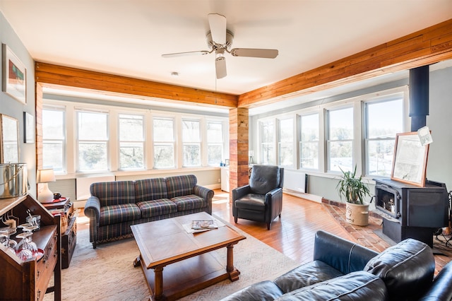 living area featuring wooden walls, a ceiling fan, light wood-style flooring, and a wood stove