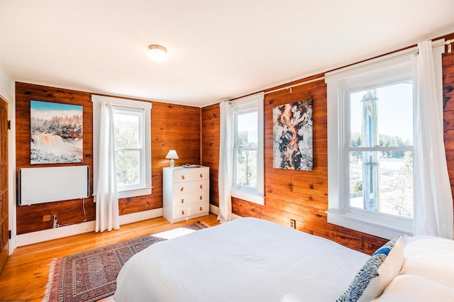 bedroom with baseboards, multiple windows, wood walls, and wood finished floors