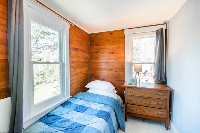 bedroom featuring light colored carpet, wood walls, and multiple windows