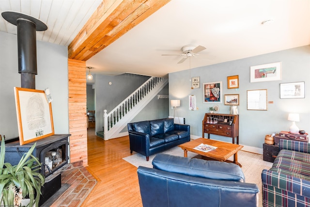 living area with a wood stove, stairs, ceiling fan, and wood finished floors