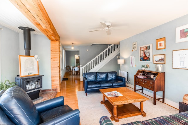 living area with a wood stove, a ceiling fan, baseboards, wood finished floors, and stairway
