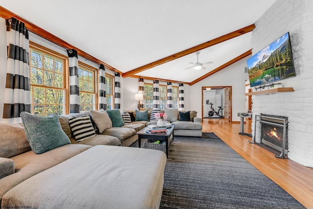 living area with ceiling fan, a large fireplace, plenty of natural light, wood finished floors, and beamed ceiling