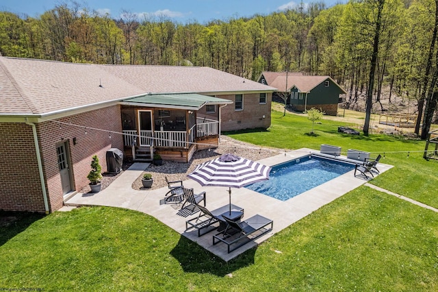 pool with a yard, a patio area, a deck, and a forest view
