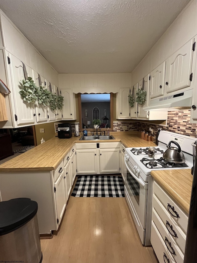 kitchen featuring white gas range, light countertops, a sink, light wood finished floors, and under cabinet range hood
