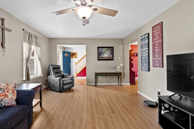 living room featuring baseboards, ceiling fan, stairs, and light wood-style flooring