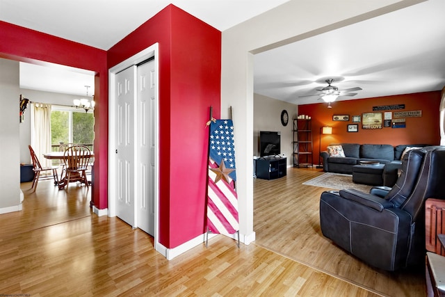 living area with light wood-style floors, baseboards, and ceiling fan with notable chandelier