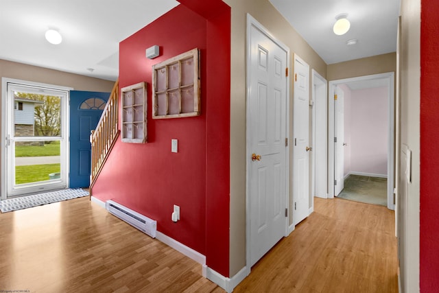 hallway featuring stairway, baseboards, light wood finished floors, and a baseboard radiator