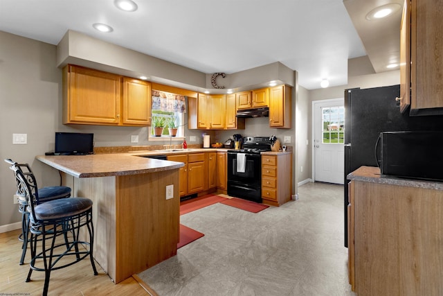 kitchen with plenty of natural light, black appliances, a peninsula, a breakfast bar, and under cabinet range hood