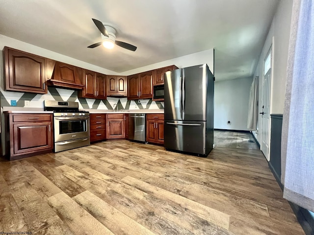 kitchen with premium range hood, light wood-type flooring, light countertops, a ceiling fan, and stainless steel appliances